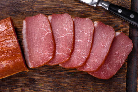 Delicious smoked meat cut with slices on a wooden cutting board against a dark grey concrete backgroundの写真素材