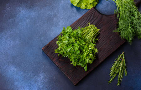Salad, parsley and dill on a dark cutting board against a blue concrete background. Cooking a...