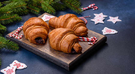 Crispy chocolate croissant with Christmas decorations on wooden cutting board on dark concrete backgroundの写真素材