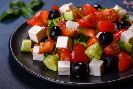 Fresh greek salad with tomato, cucumber, bel pepper, olives and feta cheese on black plateの写真素材