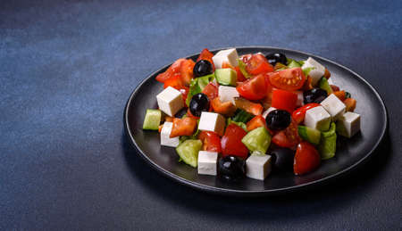 Fresh greek salad with tomato, cucumber, bel pepper, olives and feta cheese on black plateの写真素材