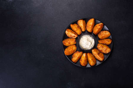 Baked potato wedges with cheese and herbs and tomato sauce on a dark background - homemade organic...