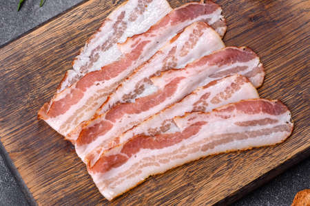Raw smoked bacon on a wooden board with several cut pieces