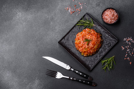 Boiled rice with peppers, spices, herbs and tomato sauce on a black slate plate on a gray concrete backgroundの写真素材