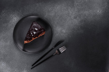 A piece of fresh delicious cake with nuts and chocolate on a black plate against a dark blue background. Desserts and sweets to the dinner tableの写真素材