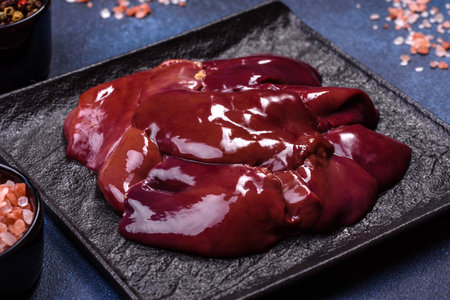Pieces of raw liver on a wooden cutting board against a dark concrete background. Preparation of liver pateの写真素材