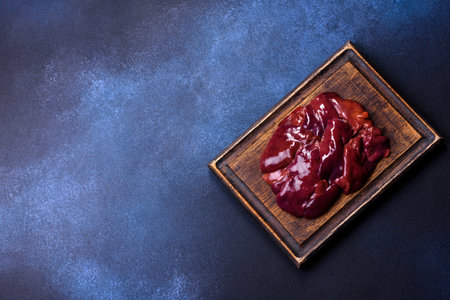 Pieces of raw liver on a wooden cutting board against a dark concrete background. Preparation of liver pateの写真素材