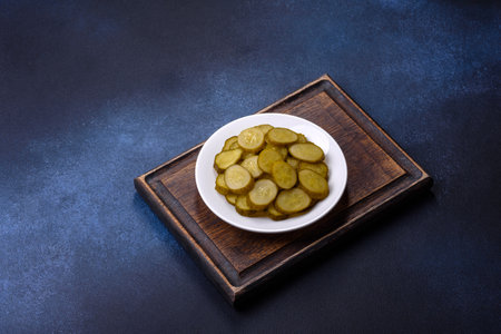 Delicious salted, canned cucumbers cut into slices on a white ceramic plate against a dark concrete backgroundの写真素材