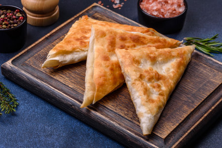 Homemade fried chebureks with meat and herbs on a cutting board on a dark concrete background, traditional Caucasian cuisineの写真素材