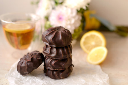Beautiful delicious chocolate marshmallows on a white table with lemon and tea against the background of white flowers in a vaseの写真素材
