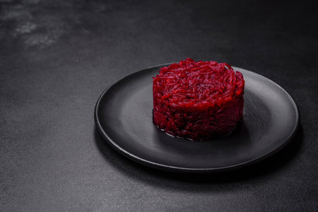Cooked grated beetroot formed as a cylinder and ready dish on a black plate against a dark concrete backgroundの写真素材