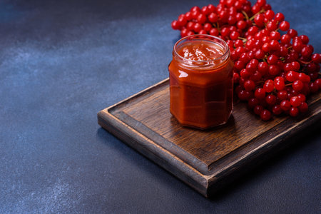 Viburnum fruit jam in a glass jar on a dark concrete background near the ripe red viburnum berries. Source of natural vitaminsの写真素材