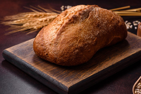 A loaf of brown bread with grains of cereals on a wooden cutting board on a dark concrete backgroundの写真素材