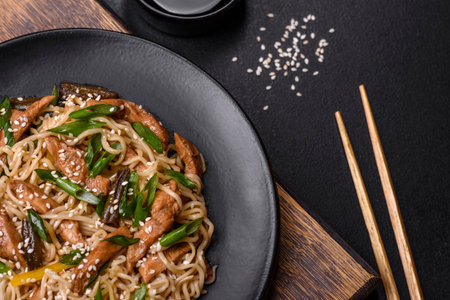 Tasty dish of Asian cuisine with rice noodles, chicken, asparagus, pepper, sesame seeds and soy sauce on dark concrete backgroundの写真素材