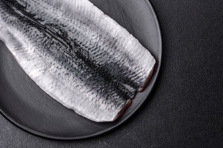Marinated fillet with spices and herbs of sea herring on a black plate against a dark concrete backgroundの写真素材