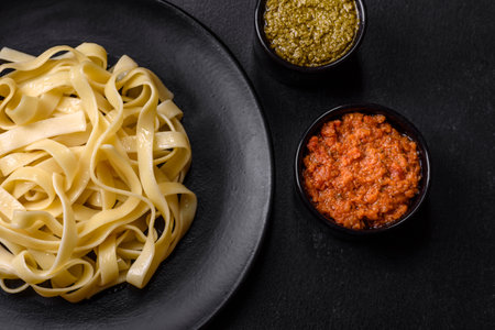 Delicious fresh pasta with pesto sauce and seafood on a black plate against a dark concrete...