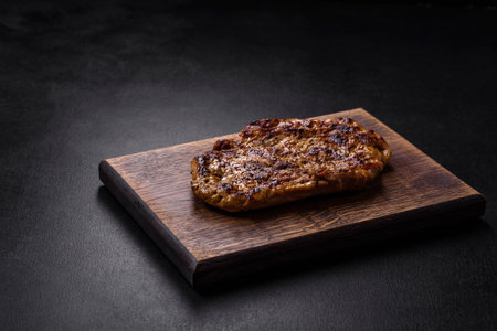 Delicious juicy grilled pork steak with spices and herbs on a wooden cutting boardの写真素材