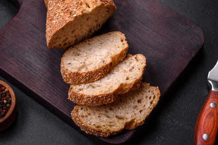 Delicious crispy bread with cereals cut into slices on a wooden cutting board on a dark concrete...
