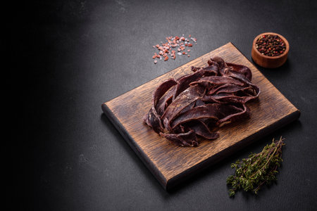Delicious salted dried beef cut into slices as an appetizer for beer on a dark concrete backgroundの写真素材