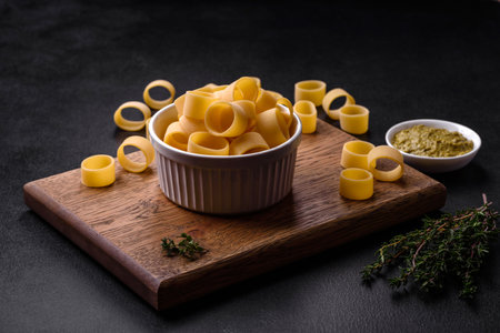 Raw uncooked pasta in a white ceramic bowl with spices and herbs on a dark concrete backgroundの写真素材