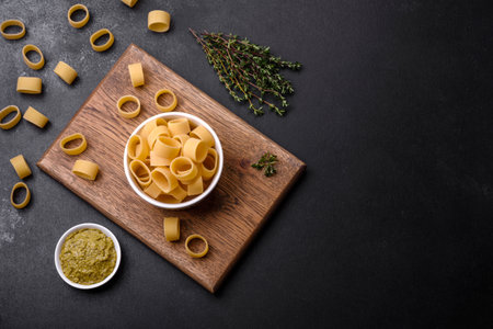 Raw uncooked pasta in a white ceramic bowl with spices and herbs on a dark concrete backgroundの写真素材