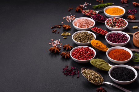 Composition consisting of variations of spices in white bowls and metal spoons on a dark concrete backgroundの写真素材