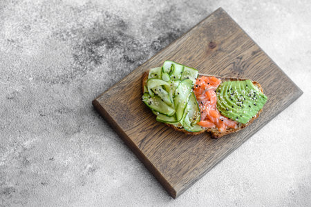 Delicious brown bread toast with salmon, avocado, cucumber and sesame seeds on a textured concrete...