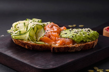 Delicious brown bread toast with salmon, avocado, cucumber and sesame seeds on a textured concrete backgroundの写真素材