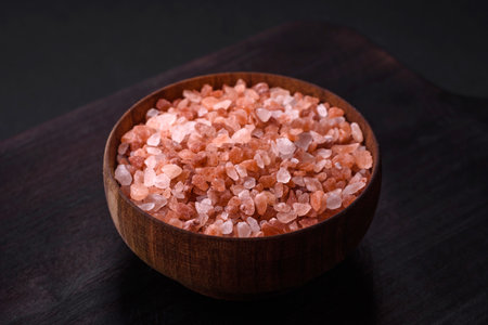 Pink himalayan salt in a wooden bowl on a dark concrete background. Seasonings and additives in the...