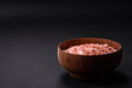 Pink himalayan salt in a wooden bowl on a dark concrete background. Seasonings and additives in the kitchenの写真素材