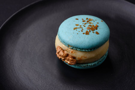 Beautiful tasty macaron with filling and fruit flavor on a black plate on a dark concrete background