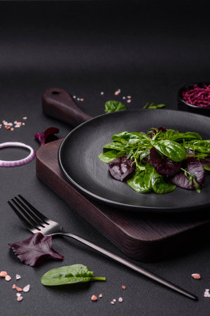 Delicious fresh salad consisting of spinach, chard, radicchio, red chart, bulls blood and arugula on a black plate on a dark concrete backgroundの写真素材