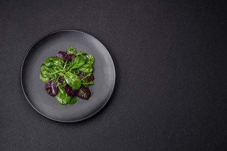 Delicious fresh salad consisting of spinach, chard, radicchio, red chart, bulls blood and arugula on a black plate on a dark concrete backgroundの写真素材