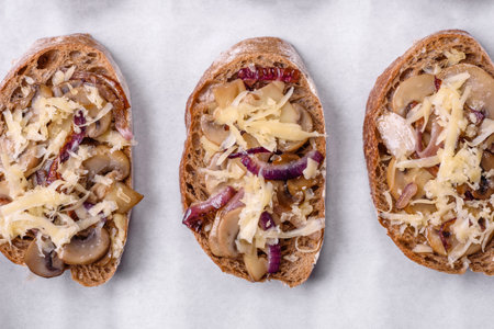 Delicious crispy toast or bruschetta with fried onion, champignon mushrooms and cheese with spices and herbs on a dark concrete backgroundの写真素材