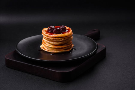 Delicious fresh pancakes with berry jam on a black ceramic plate on a dark concrete background