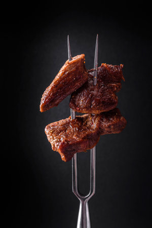 Several pieces of fresh grilled beef with spices and herbs and strung on a fork on a dark concrete backgroundの写真素材