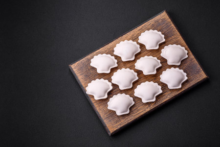 Raw frozen stuffed dumplings on a wooden cutting board on a dark concrete backgroundの写真素材
