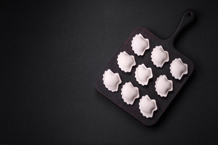 Raw frozen stuffed dumplings on a wooden cutting board on a dark concrete background