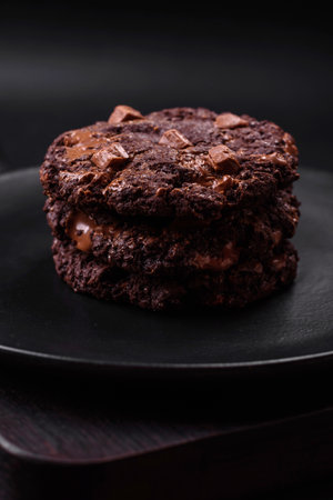 Delicious fresh oatmeal round cookies with chocolate on a black ceramic plate on a dark concrete backgroundの写真素材