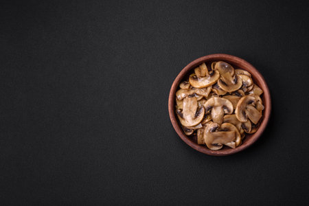 Fried or stewed champignon mushrooms in the form of slices with onions on a brown ceramic plate on a dark concrete backgroundの写真素材