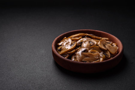 Fried or stewed champignon mushrooms in the form of slices with onions on a brown ceramic plate on a dark concrete backgroundの写真素材
