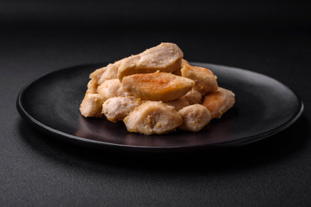 Delicious chicken slices baked with spices and herbs on a round ceramic plate on a dark concrete backgroundの写真素材