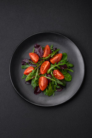 Salad of fresh cherry tomatoes, arugula, spinach, young beet leaves and other greens on a dark concrete backgroundの写真素材