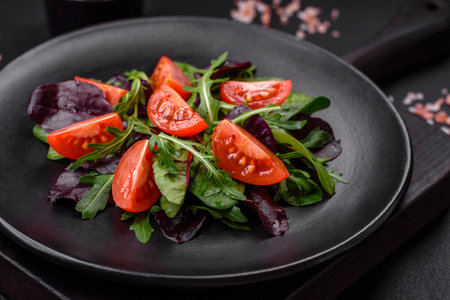 Salad of fresh cherry tomatoes, arugula, spinach, young beet leaves and other greens on a dark concrete backgroundの写真素材