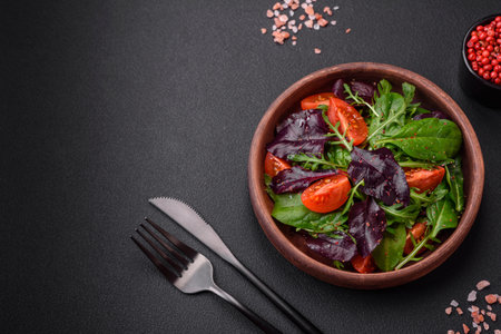 Salad of fresh cherry tomatoes, arugula, spinach, young beet leaves and other greens on a dark concrete backgroundの写真素材