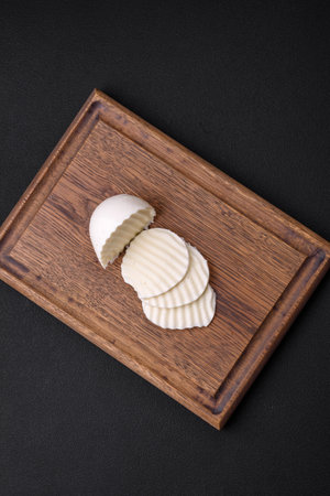 Delicious fresh mozzarella cut into slices on a wooden cutting board on a dark concrete backgroundの写真素材
