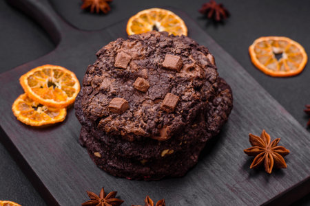 Delicious fresh crispy oatmeal cookies with chocolate and nuts on a black ceramic plate on a dark concrete backgroundの写真素材