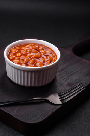 Delicious canned beans in a tomato in a white ceramic bowl on a dark concrete backgroundの写真素材