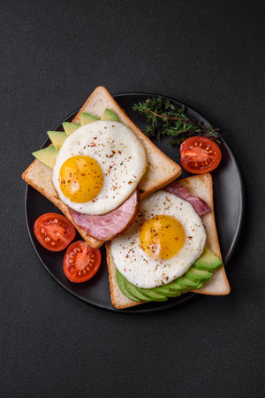 Delicious nutritious English breakfast with fried eggs, tomatoes and avocado with spices and herbs on a dark concrete backgroundの写真素材