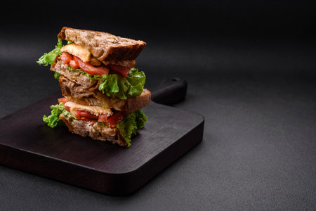 Delicious sandwich with crispy toast, chicken, tomatoes and lettuce on a dark concrete backgroundの写真素材